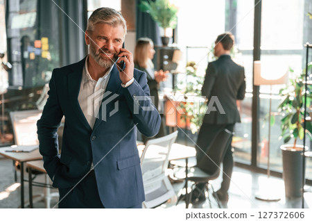 Man is standing and having phone call. Group of business people are working in the modern office Man is standing and having phone call. Group of business people are working in the modern office 127372606