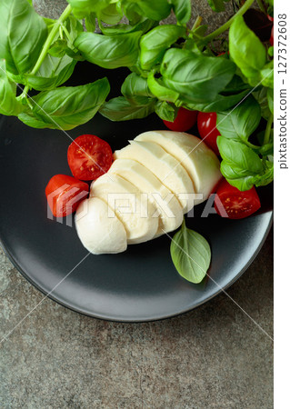 Mozzarella cheese with cherry tomatoes and basil on a stone table. 127372608
