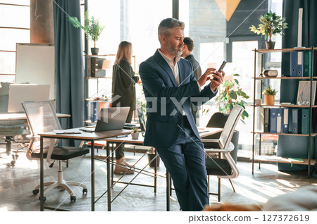 Man is leaning on the table. With smartphone in hands. Group of business people are working in the modern office 127372619