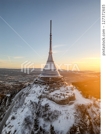 Jested Mountain showcases a stunning winter landscape illuminated by the soft light of sunrise. Snow blankets the peaks, creating a serene and tranquil atmosphere. 127372685