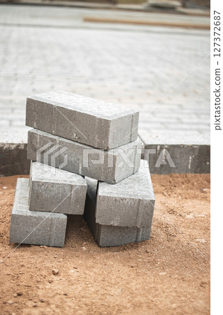 Stacked gray concrete blocks on a construction site with a paved area in the background 127372687