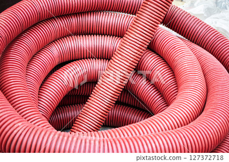 Bright red flexible tubes coiled together in a construction site in the afternoon sunlight 127372718