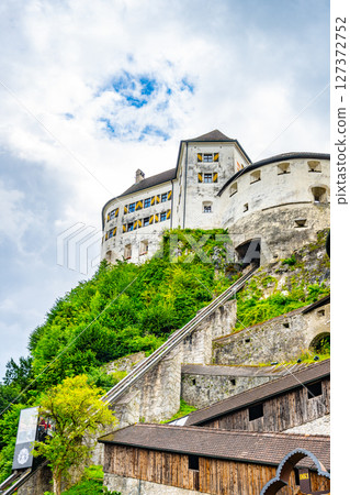 Kufstein Fortress stands majestically atop a hill in Tyrol, Austria, showcasing its historical architecture. Lush greenery surrounds the fortress, contrasting with the cloudy sky. 127372752