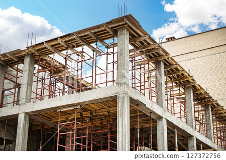 Construction site with scaffolding and unfinished building under blue sky and clouds Construction site with scaffolding and unfinished building under blue sky and clouds 127372756