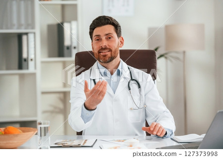 In white coat, sitting. Doctor in formal clothes is working in the cabinet 127373998