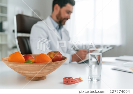 Fruits is on the table. Doctor in formal clothes is working in the cabinet Fruits is on the table. Doctor in formal clothes is working in the cabinet 127374004