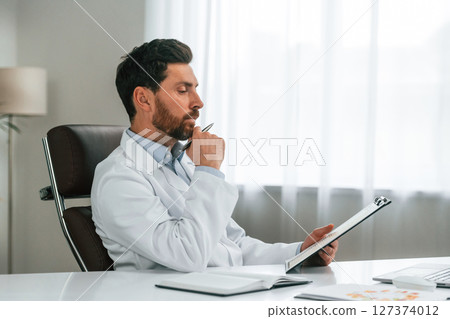 Reading the document. Doctor in formal clothes is working in the cabinet Reading the document. Doctor in formal clothes is working in the cabinet 127374012