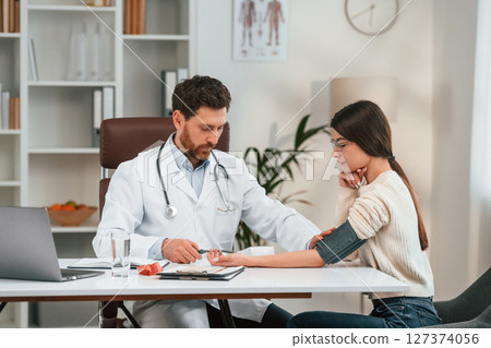 Measuring blood pressure. With woman. Doctor in formal clothes is working in the cabinet Measuring blood pressure. With woman. Doctor in formal clothes is working in the cabinet 127374056