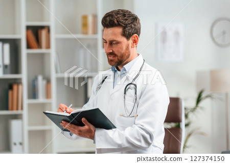 With notepad. Doctor in formal clothes is working in the cabinet With notepad. Doctor in formal clothes is working in the cabinet 127374150