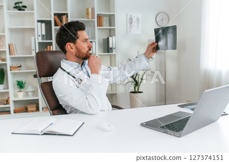 Looking at x-ray. Doctor in formal clothes is working in the cabinet Looking at x-ray. Doctor in formal clothes is working in the cabinet 127374151