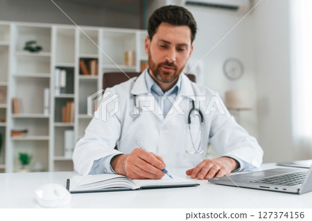 Sitting by a table. Doctor in formal clothes is working in the cabinet 127374156