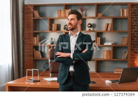Standing with arms crossed. Businessman in formal clothes is working indoors Standing with arms crossed. Businessman in formal clothes is working indoors 127374164