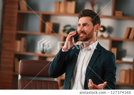 Active conversation by phone. Businessman in formal clothes is working indoors Active conversation by phone. Businessman in formal clothes is working indoors 127374168