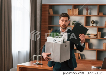 With a box of stuff in it. Businessman in formal clothes is working indoors With a box of stuff in it. Businessman in formal clothes is working indoors 127374173