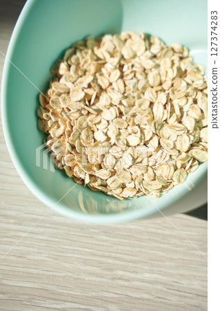 Healthy breakfast flat lay of raw oats in a green bowl on light wooden table 127374283