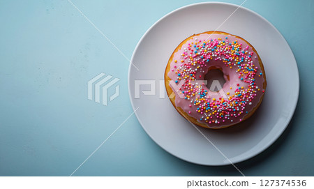 Pink glazed donut with colorful sugar sprinkles on a white plate over a blue background. Banner with copy space. 127374536