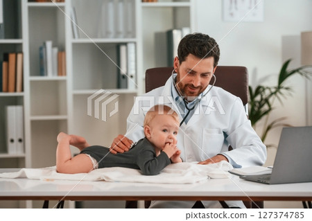 With stethoscope. Doctor with little baby is working in the cabinet With stethoscope. Doctor with little baby is working in the cabinet 127374785