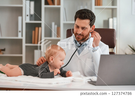 With stethoscope. Doctor with little baby is working in the cabinet With stethoscope. Doctor with little baby is working in the cabinet 127374786