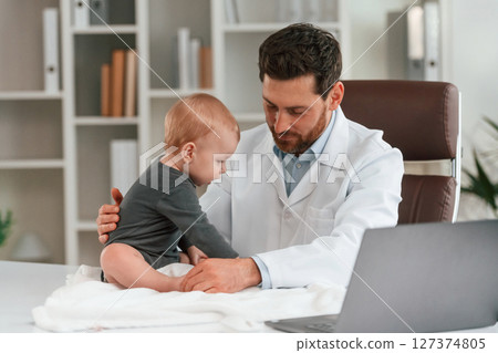 Checking the legs. Doctor with little baby is working in the cabinet Checking the legs. Doctor with little baby is working in the cabinet 127374805