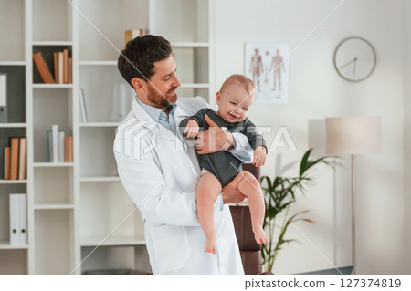 Standing and holding boy. Doctor with little baby is working in the cabinet Standing and holding boy. Doctor with little baby is working in the cabinet 127374819
