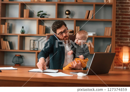 Work and family. Businessman in formal clothes is indoors. With toddler Work and family. Businessman in formal clothes is indoors. With toddler 127374859