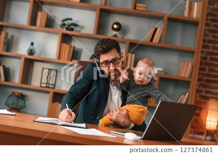 Work and family. Businessman in formal clothes is indoors. With toddler Work and family. Businessman in formal clothes is indoors. With toddler 127374861