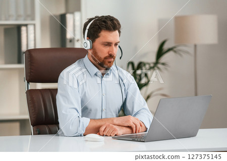 In headphones. Doctor in formal clothes is working in the cabinet In headphones. Doctor in formal clothes is working in the cabinet 127375145