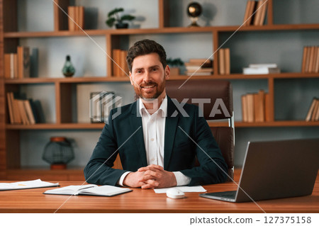 Sitting by table with laptop. Businessman in formal clothes is working indoors 127375158