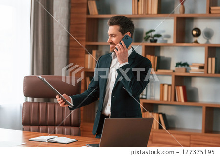Talking by phone. Businessman in formal clothes is working indoors Talking by phone. Businessman in formal clothes is working indoors 127375195