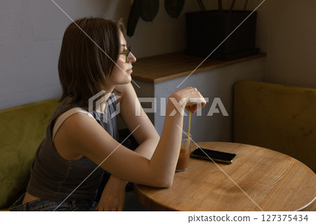 woman is sitting in a cafe with a glass of orange coffee and looking out the window. woman is sitting in a cafe with a glass of orange coffee and looking out the window. 127375434