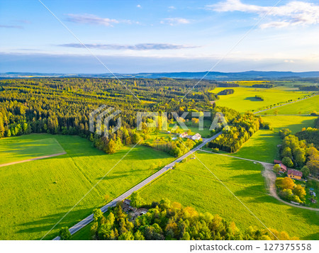 A stunning view of lush green fields under a vibrant sky during a spring evening. Gentle hills and forests frame the scene, creating a tranquil rural atmosphere. 127375558