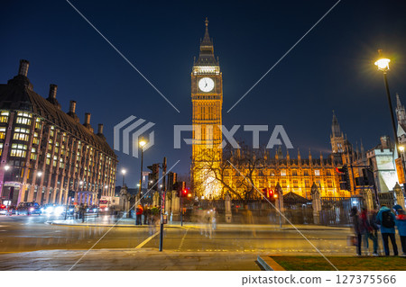 Crowds of people navigate the streets near Big Ben and Westminster Palace as night falls in London. The illuminated clock tower stands tall against the evening sky, enhancing the bustling atmosphere. Crowds of people navigate the streets near Big Ben and Westminster Palace as night falls in London. The illuminated clock tower stands tall against the evening sky, enhancing the bustling atmosphere. 127375566