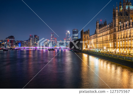 Brightly lit Palace of Westminster stands majestically at night alongside the Thames River, with the modern Vauxhall skyscrapers shining in the background, showcasing London's vibrant skyline. Brightly lit Palace of Westminster stands majestically at night alongside the Thames River, with the modern Vauxhall skyscrapers shining in the background, showcasing London's vibrant skyline. 127375567