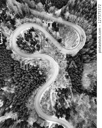 A serpentine road twists through a dense forest, showcasing the contrast between the smooth curves and the rugged terrain. The aerial perspective enhances the beauty of nature. A serpentine road twists through a dense forest, showcasing the contrast between the smooth curves and the rugged terrain. The aerial perspective enhances the beauty of nature. 127375572