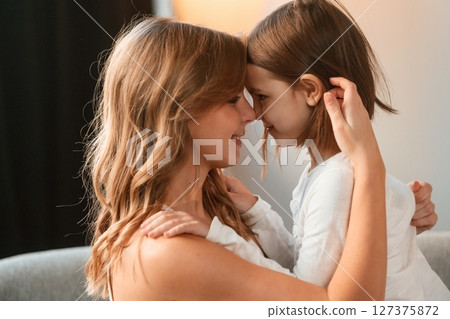 Side view, embracing each other. Mother with her little daughter is together in domestic room 127375872