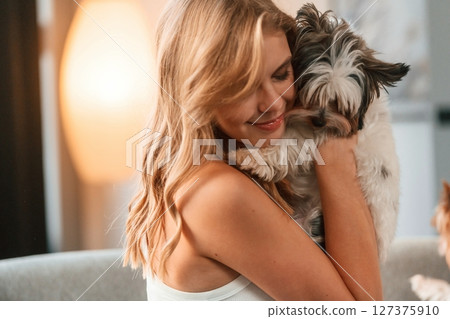 Embracing the animal. Beautiful young woman is with little dog indoors Embracing the animal. Beautiful young woman is with little dog indoors 127375910