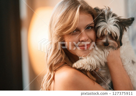 Embracing the animal. Beautiful young woman is with little dog indoors 127375911