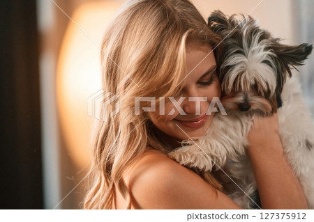 Embracing the animal. Beautiful young woman is with little dog indoors Embracing the animal. Beautiful young woman is with little dog indoors 127375912