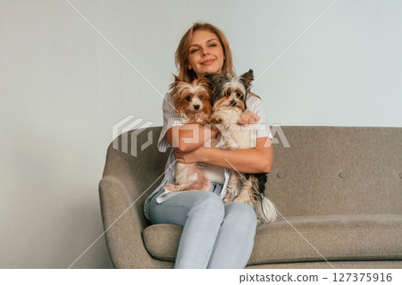 Holding and embracing the animals. Woman is sitting on a sofa with two cute dogs Holding and embracing the animals. Woman is sitting on a sofa with two cute dogs 127375916