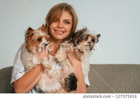 Holding and embracing the animals. Woman is sitting on a sofa with two cute dogs 127375918