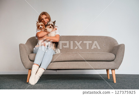 Conception of care and love. Woman is sitting on a sofa with two cute dogs 127375925