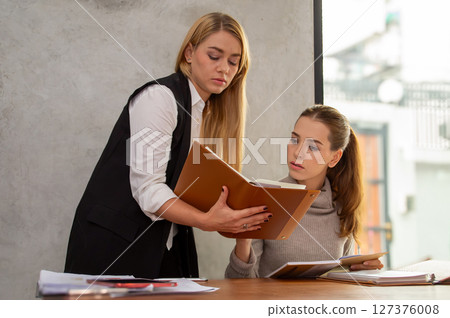 Two women engage in a productive discussion while reviewing documents in a modern office setting. Two women engage in a productive discussion while reviewing documents in a modern office setting. 127376008