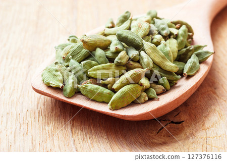 Green cardamom pods on wooden spoon Green cardamom pods on wooden spoon 127376116