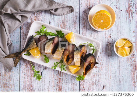 Cold smoked mackerel pieces, lemon and arugula on a plate on the table top view Cold smoked mackerel pieces, lemon and arugula on a plate on the table top view 127376300