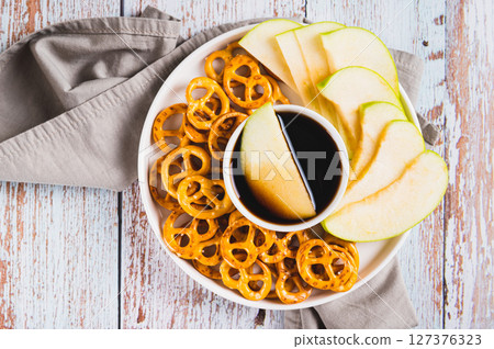 Close up of miso caramel dipping sauce, granny smith apples and pretzels on a plate top view 127376323
