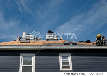 Construction Workers Installing Asphalt Shingles on Residential Roof Against Blue Sky with Clouds 127376499