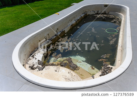 Dirty abandoned swimming pool with stagnant water and debris. 127376589