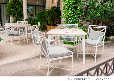 Elegant outdoor cafe terrace with white furniture and lush greenery. Relaxation, summer lifestyle, and modern hospitality. 127376652