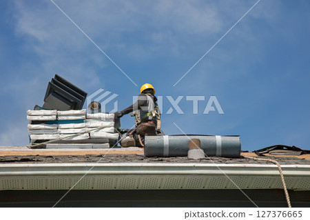 Professional Roofer in Hard Hat Installing Asphalt Shingles on Residential House Roof 127376665