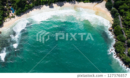 Turquoise waters kiss the beach's sandy shore, surrounded by vibrant flora. Seychelles, Mahe. Anse Louis beach. 127376857